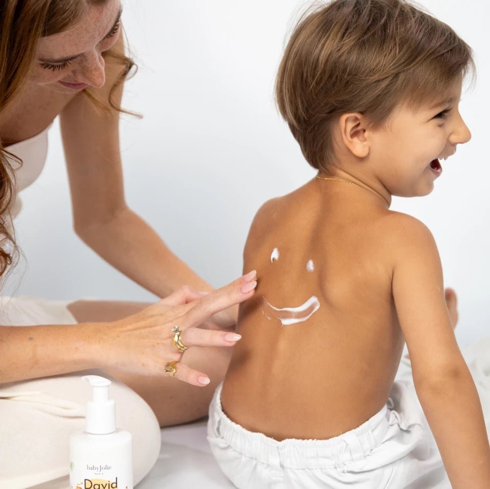 Mother applying David & Noah moisturizing lotion in a smiley face shape on a happy child's back.