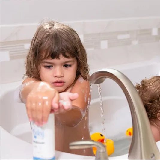 Young child in a bathtub holding a white 7.5oz bottle of Baby Jolie conditioner near a faucet and rubber ducks.