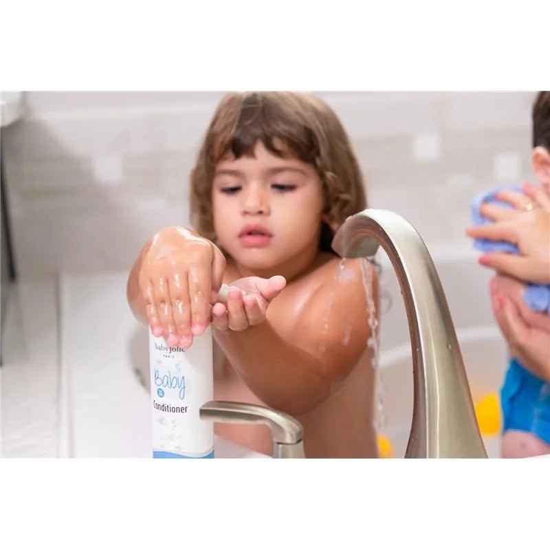 Toddler pumping Baby Jolie hair conditioner from a white 7.5oz bottle into their hands at a bathroom sink.