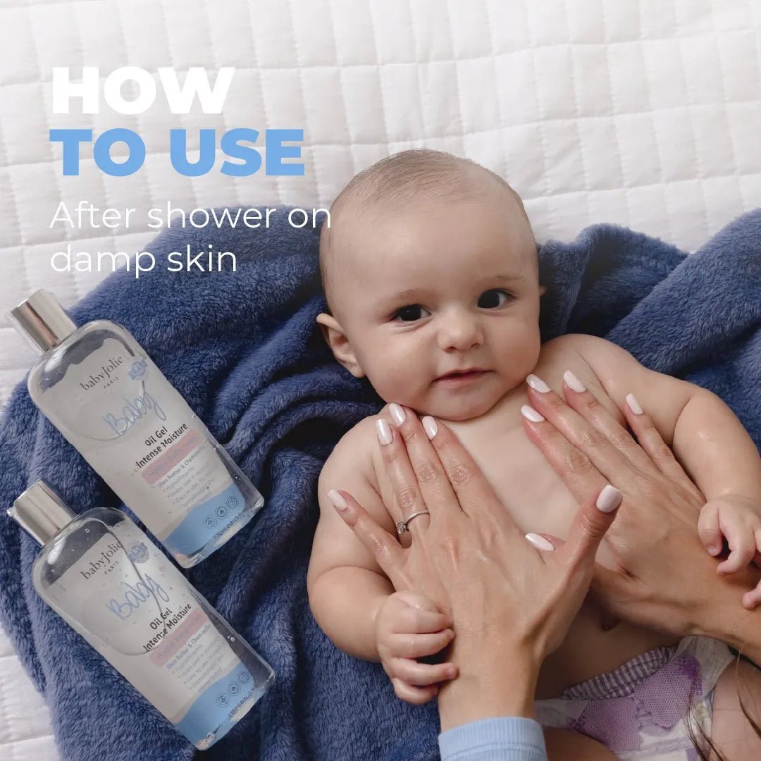 Hands applying Baby Jolie intensive moisture oil gel to a baby on a soft blue blanket.