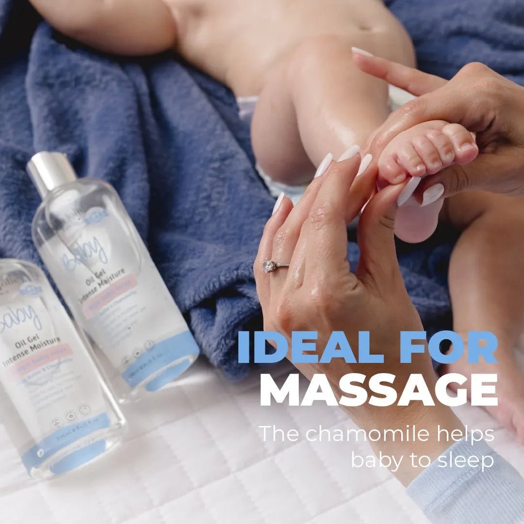 Hands massaging a baby's foot next to two clear bottles of Baby Oil Gel with blue labels on a soft blue towel.