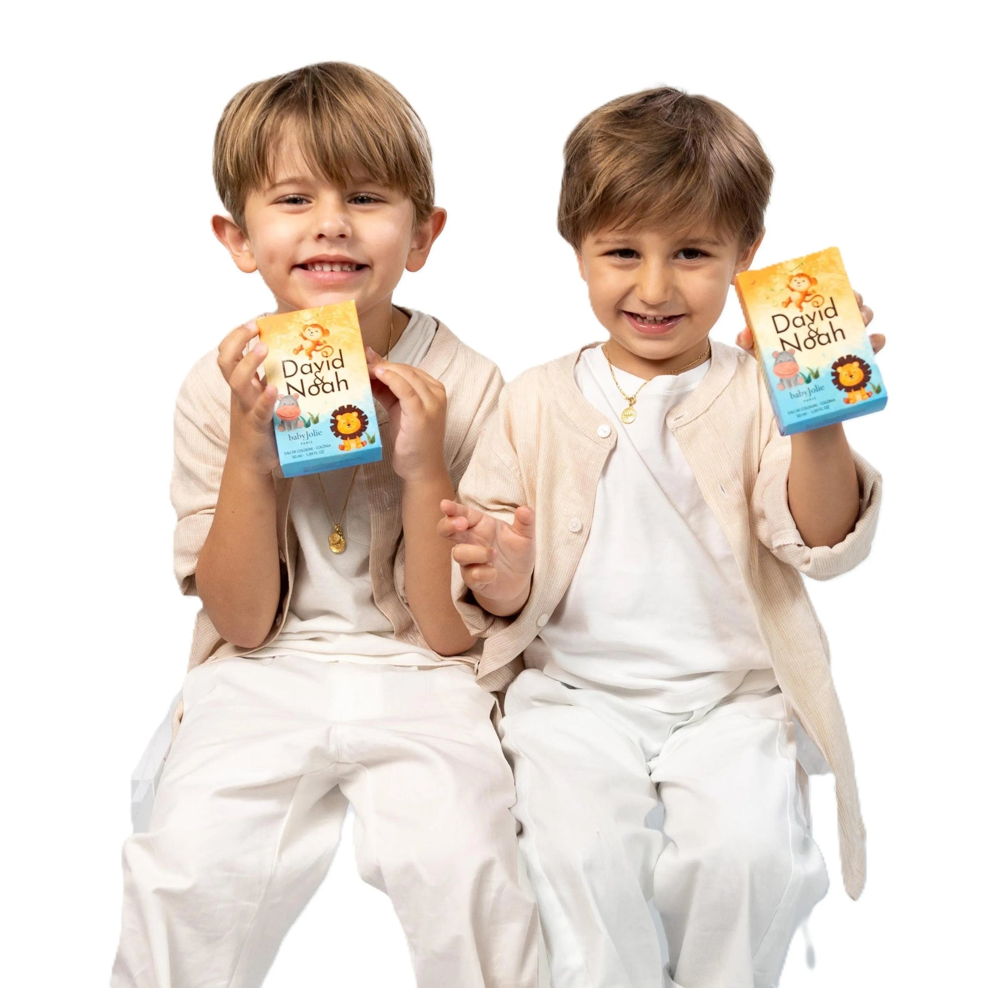 Two smiling boys in white outfits holding David & Noah kids perfume boxes with colorful animal illustrations.
