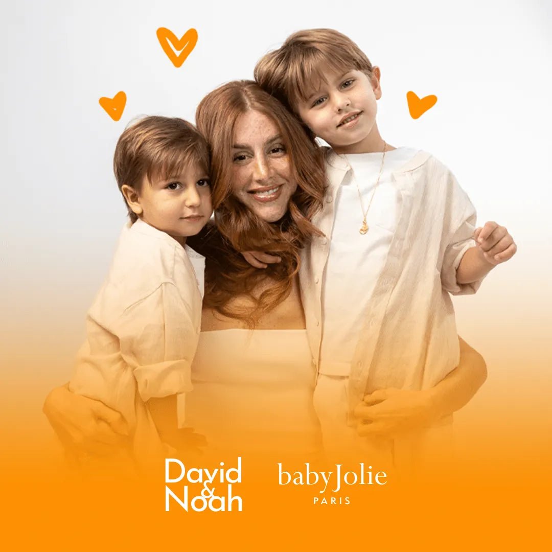 Mari Maria hugging her two sons in white outfits against an orange gradient background with heart icons and brand logos.