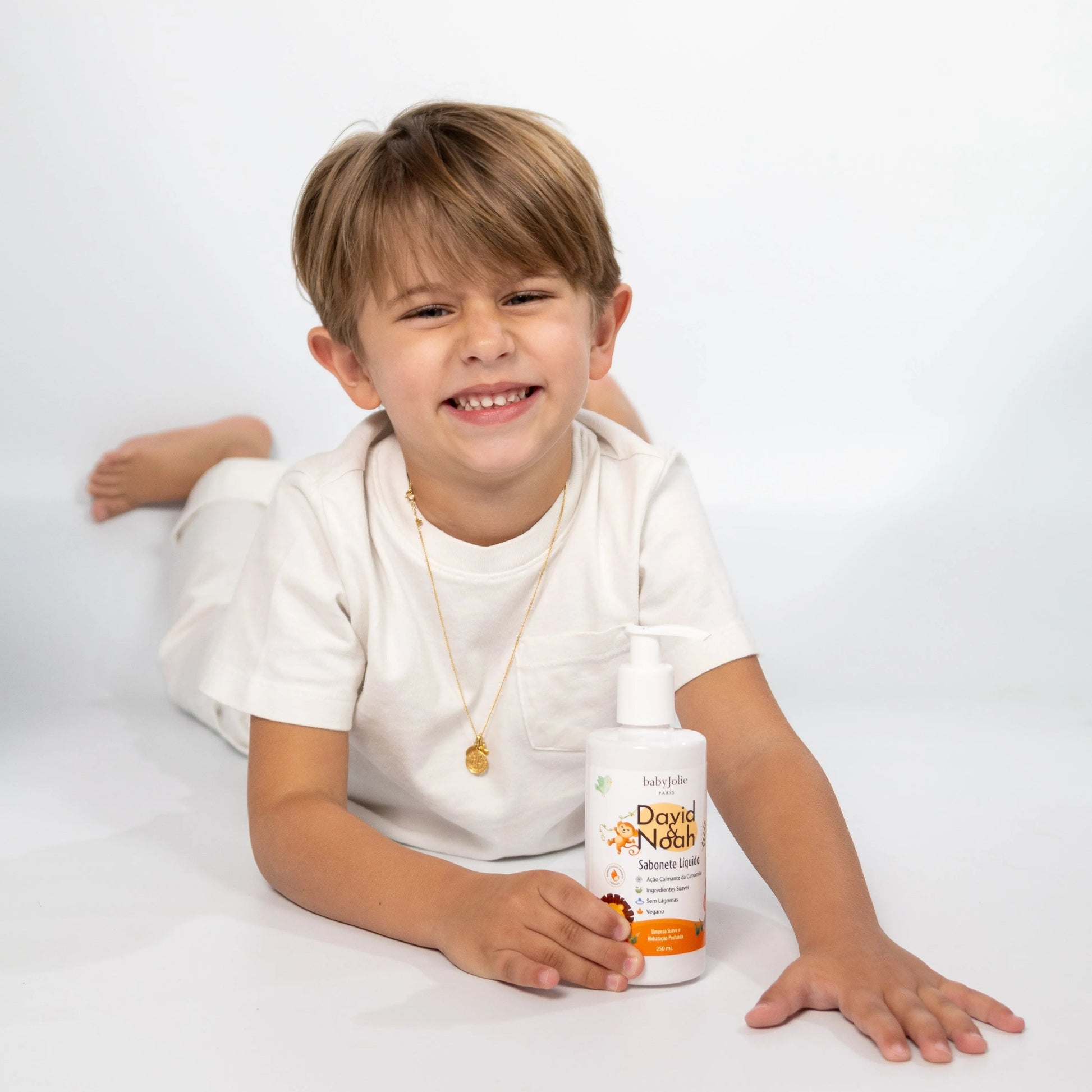 Smiling boy in a white shirt holding a white David & Noah liquid soap bottle against a clean white background.