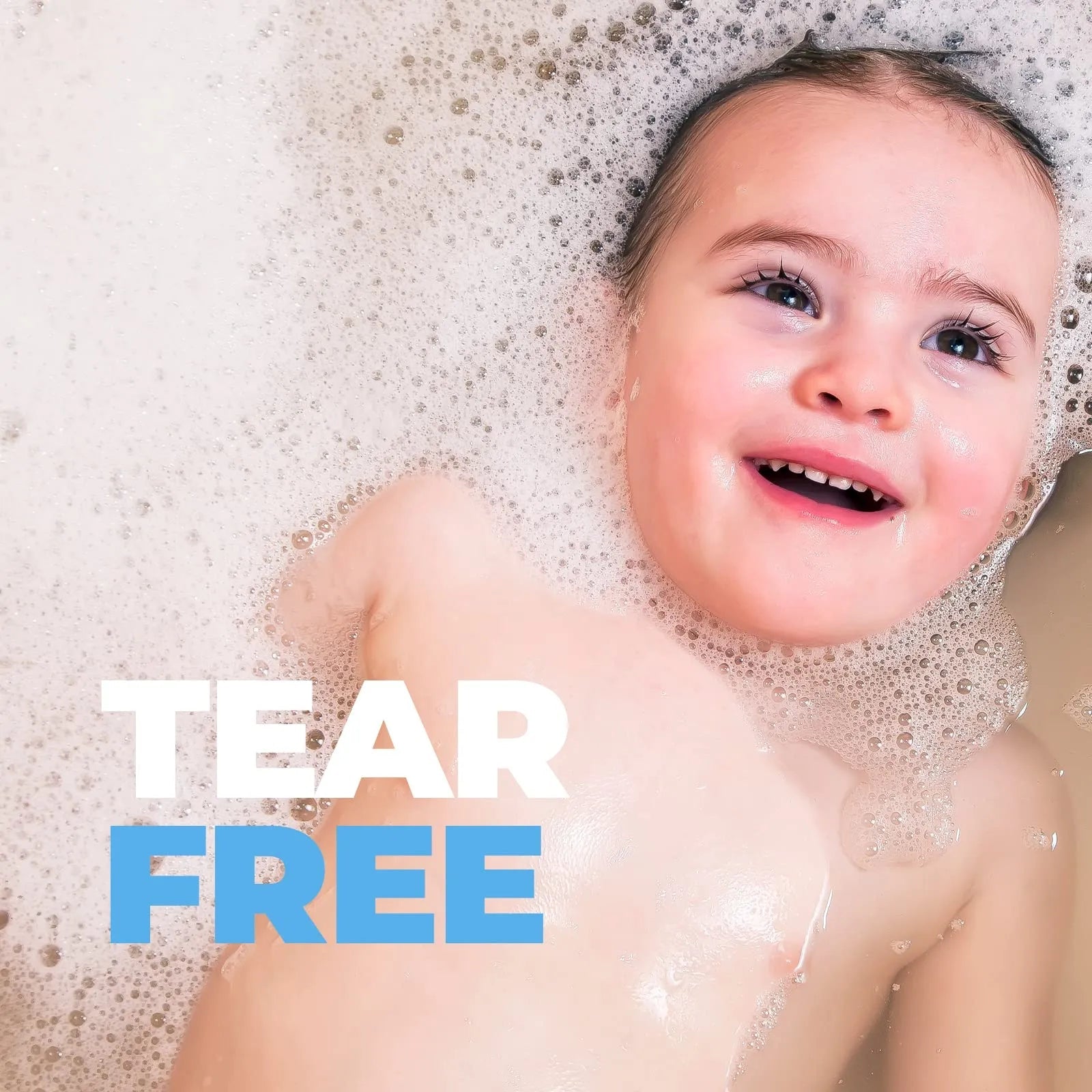 Happy baby smiling in a bubble bath with white foam, featuring bold Tear Free text overlay for gentle hair care.