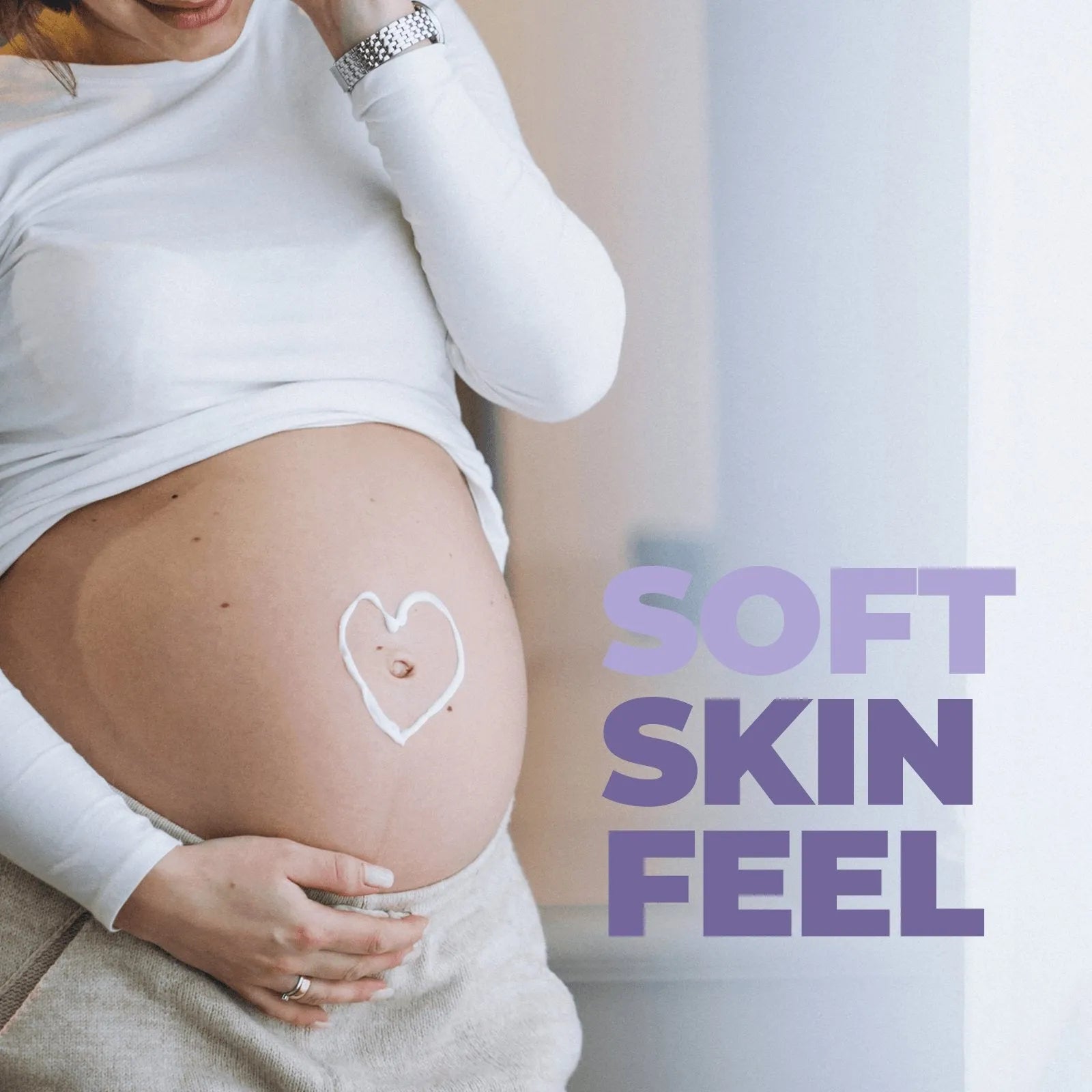 Pregnant woman in a white long-sleeve shirt with a heart drawn in cream on her belly and the text Soft Skin Feel.